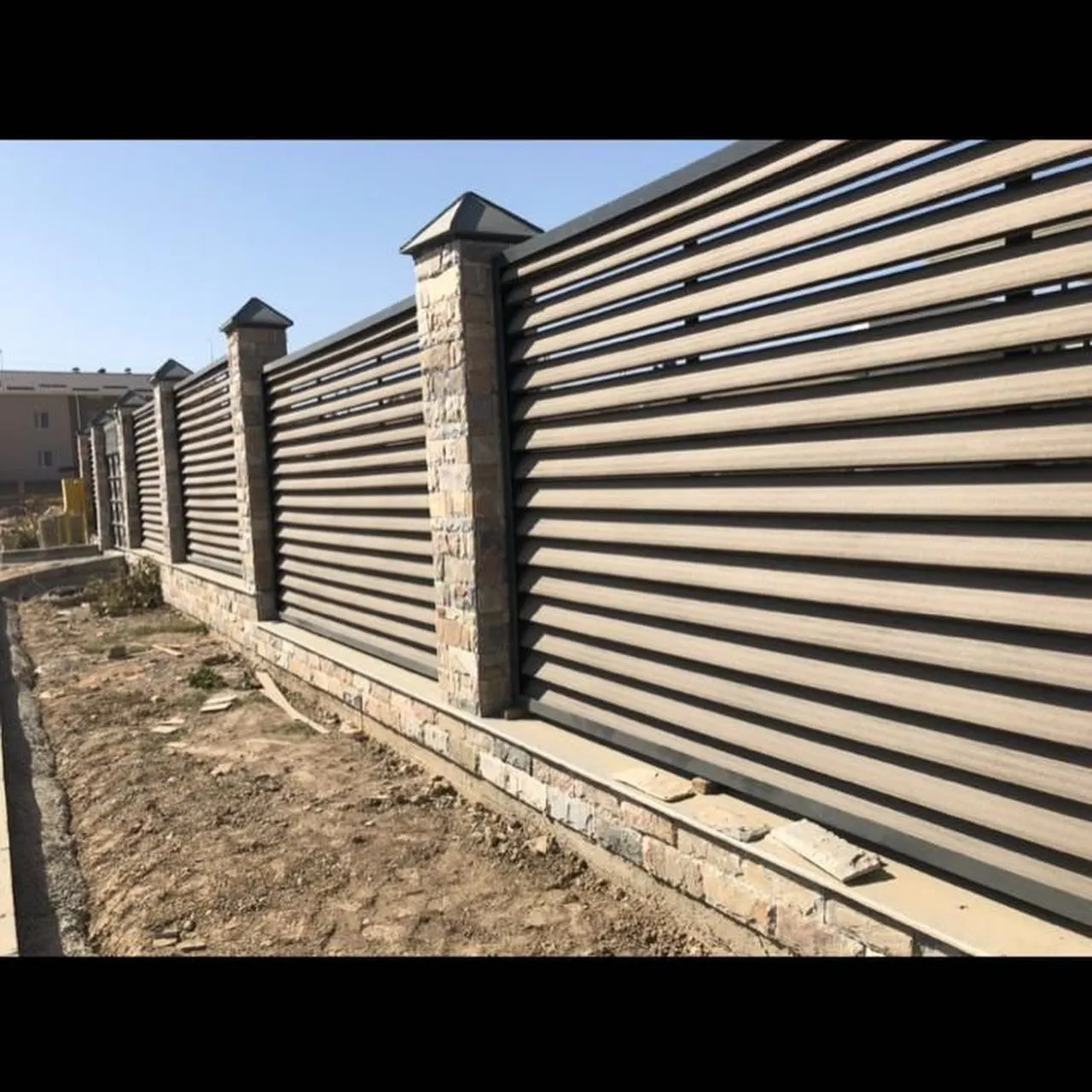Забор из горизонтальных досок ДПК песочно-бежевого цвета между столбами из облицовочного камня