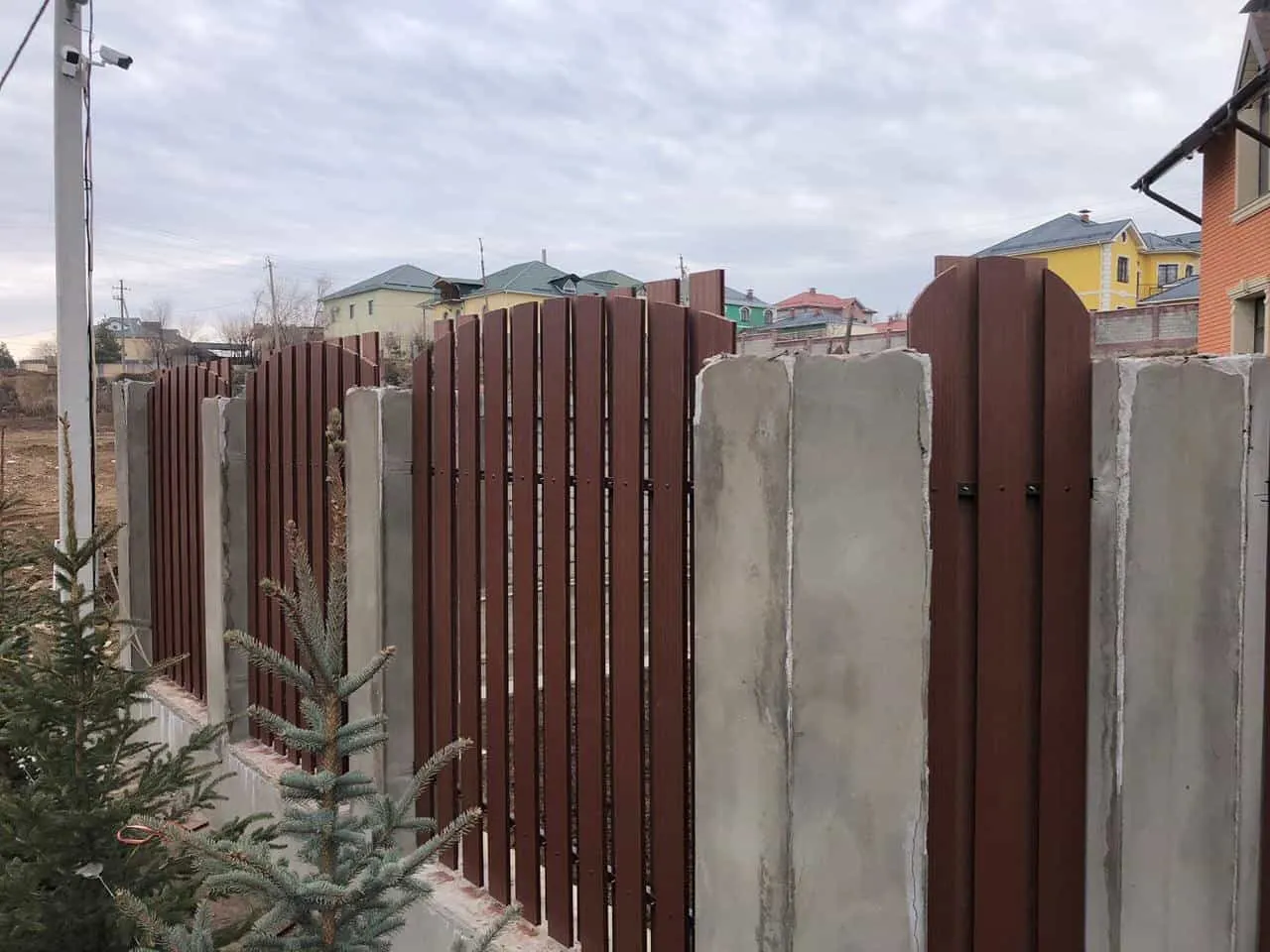 Забор из вертикальных досок на бетонных столбах: ряд стоек и досок, по которому видно, ровно ли стоит ограждение