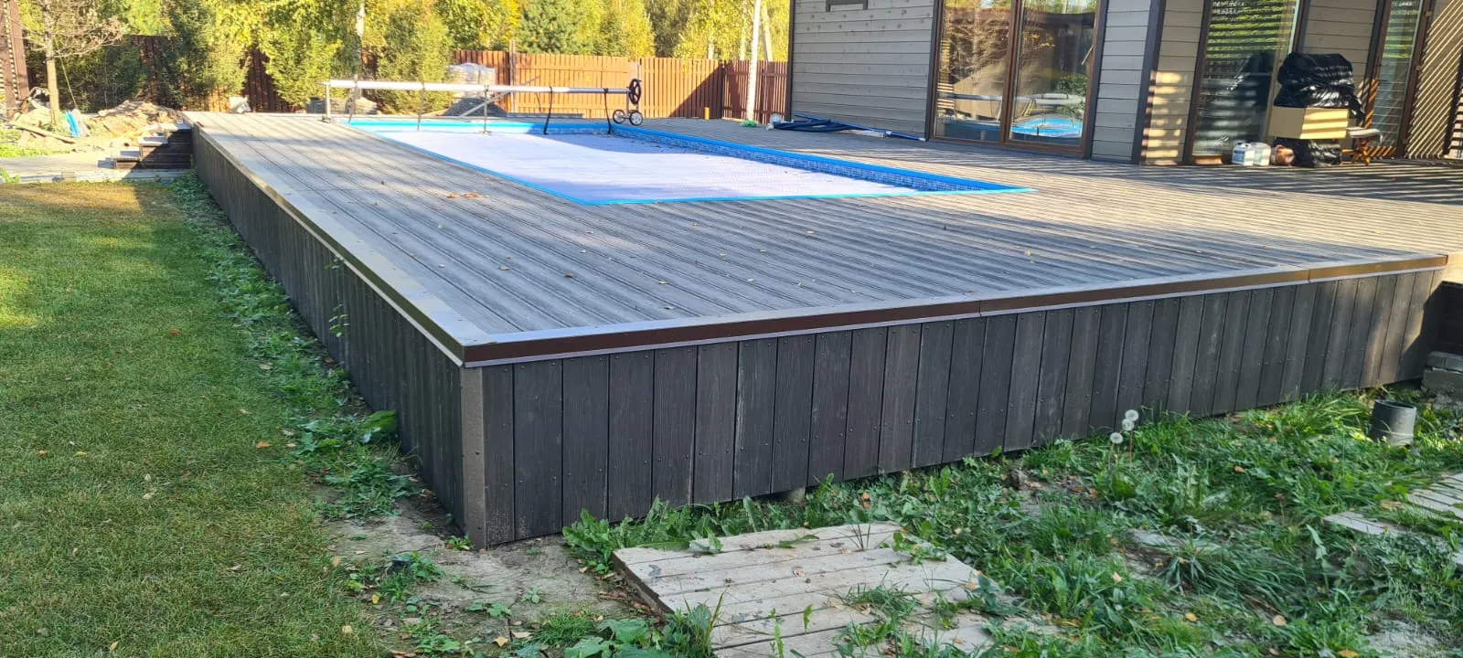Настил из ДПК над газоном на каркасе, под досками виден воздушный зазор